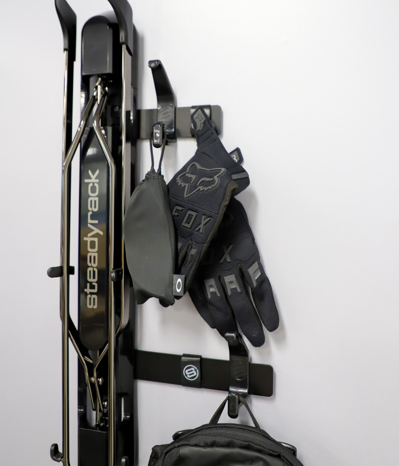 Wall mounted bike rack with Steadyrack logo, with black brackets holding gloves and a sunglasses bag. 