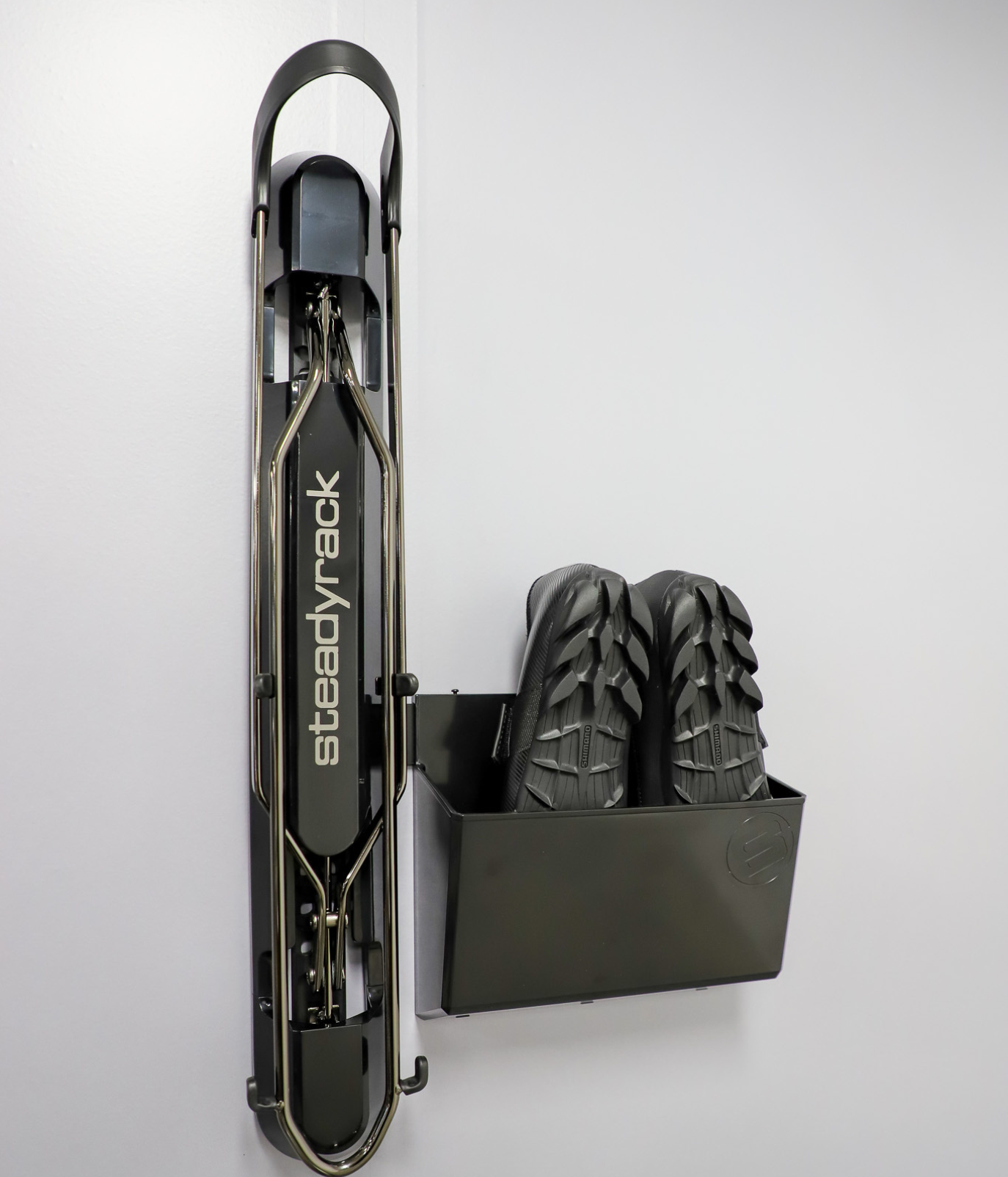 Steadyrack bike rack installed on a white wall with a large black bin storing shoes attached. 