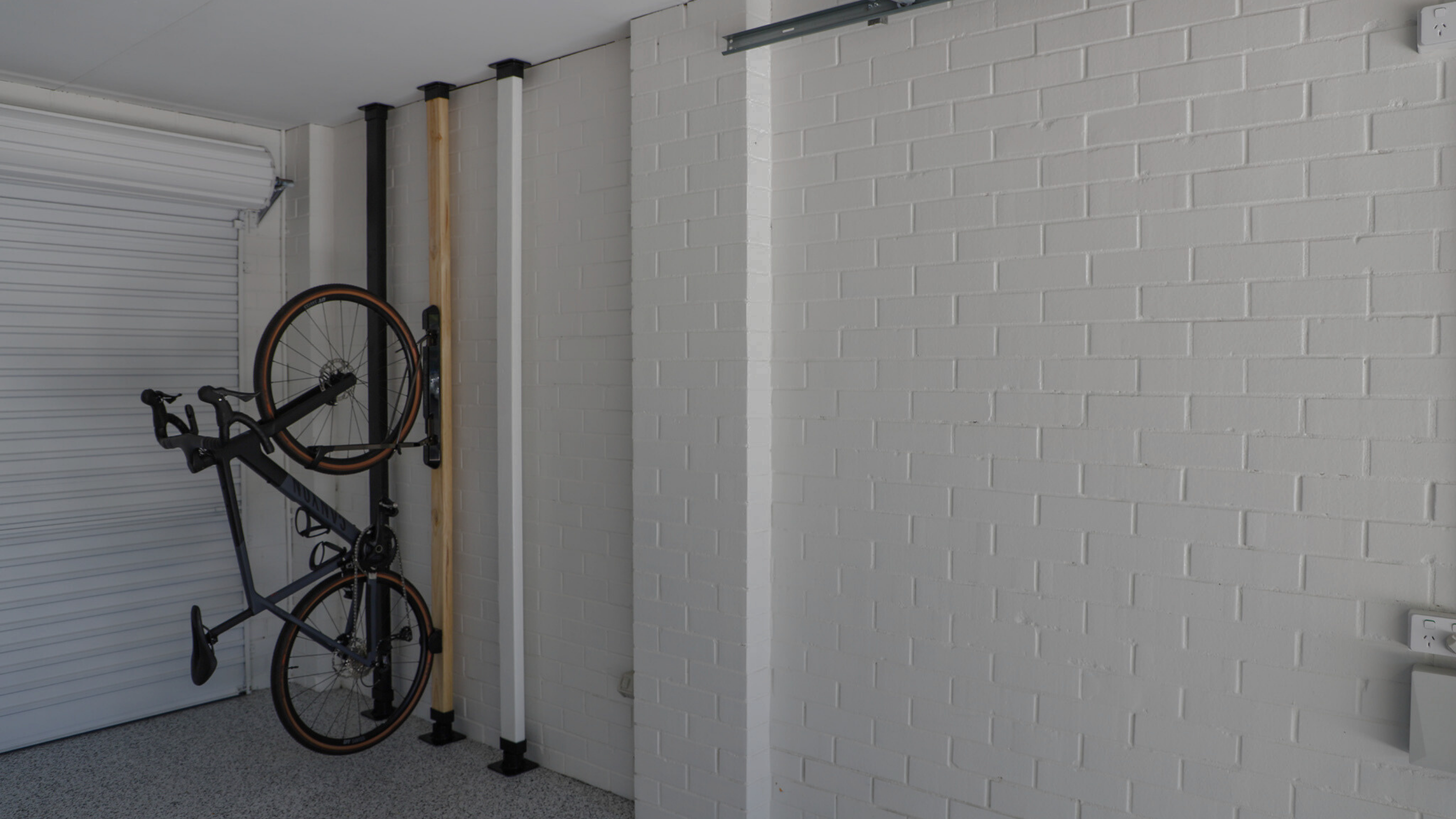 Bicycle hanging on a wall-mounted rack in a garage with white brick walls.