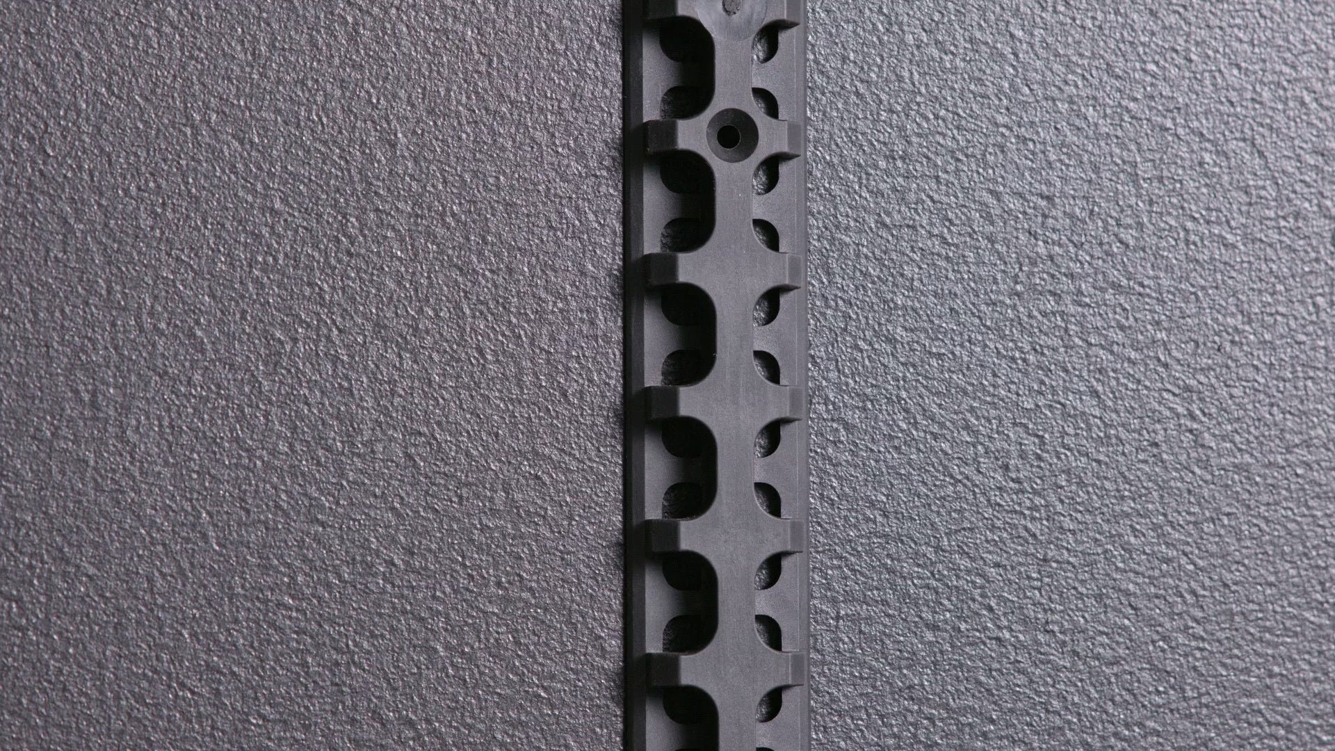 A black metal bracket being hooked into a black spine system. 