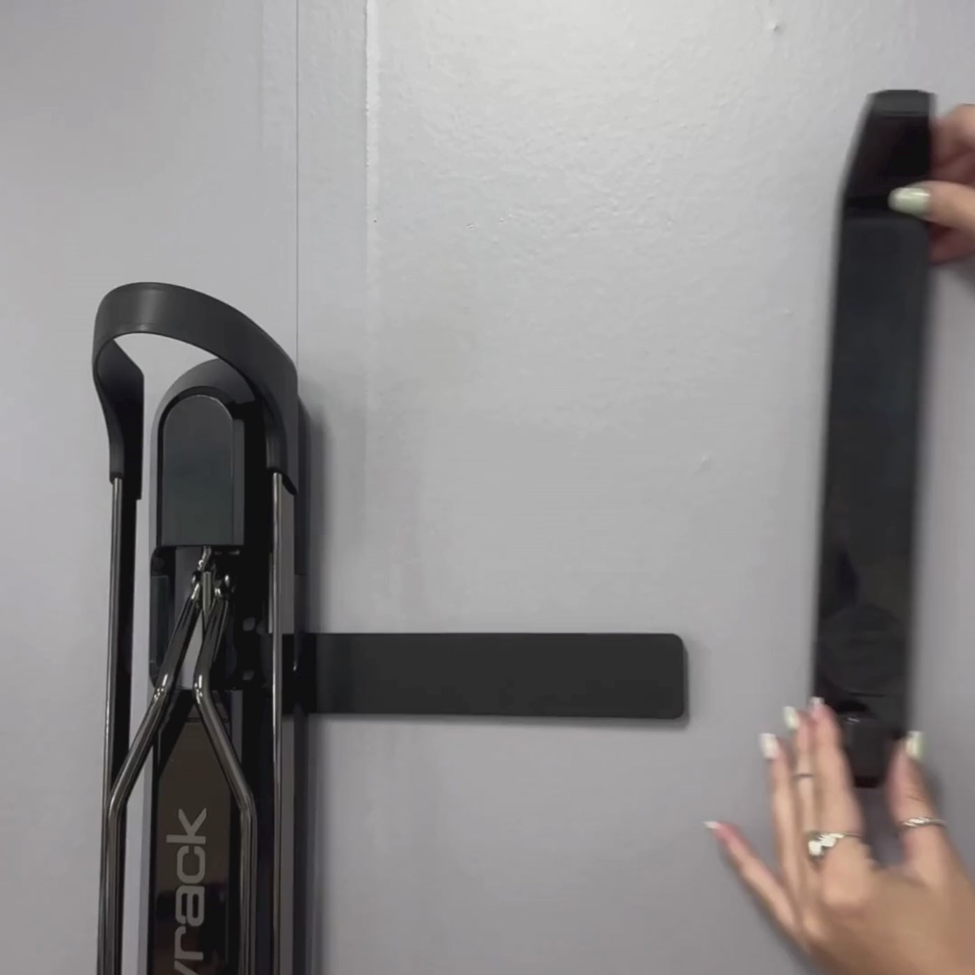 A person sliding a black helmet hooking onto a black metal bracket. 