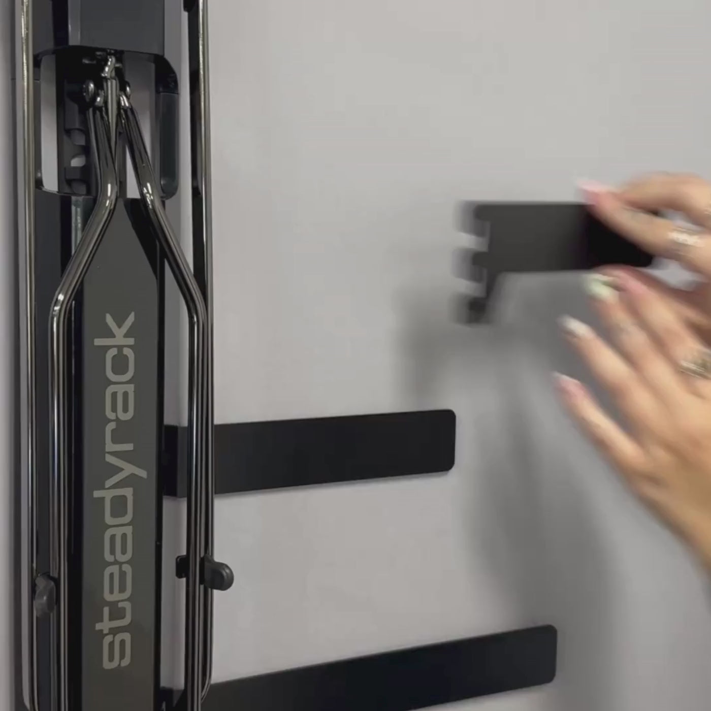 A person slotting a black metal bracket into the storage system spine that is installed behind a Steadyrack bike rack. 
